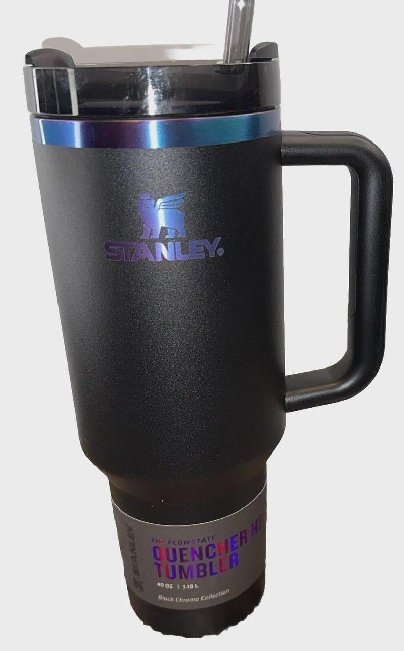 May include: Black Stanley Quencher H Tumbler with a handle and a straw. The tumbler has a black lid with a blue iridescent band. The Stanley logo is in blue. The tumbler holds 40 oz (1.18 L).