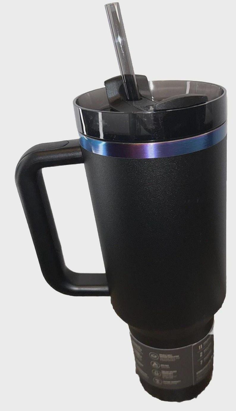 May include: Black insulated travel mug with a handle and a clear straw. The mug has a black lid with a sliding closure and a metallic blue and purple band around the middle. The mug is designed to keep beverages cold or hot.