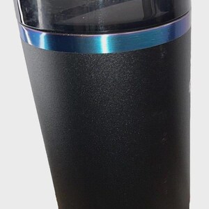 May include: Black insulated tumbler with a clear lid and a reusable straw. The tumbler has a textured surface and a blue iridescent band around the middle. The bottom portion of the tumbler is a lighter shade of black.