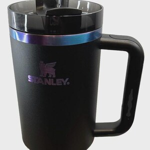 May include: Black Stanley Quencher tumbler with a handle and a clear straw. The tumbler has a black lid and a band of iridescent color around the middle. The Stanley logo is visible on the front.