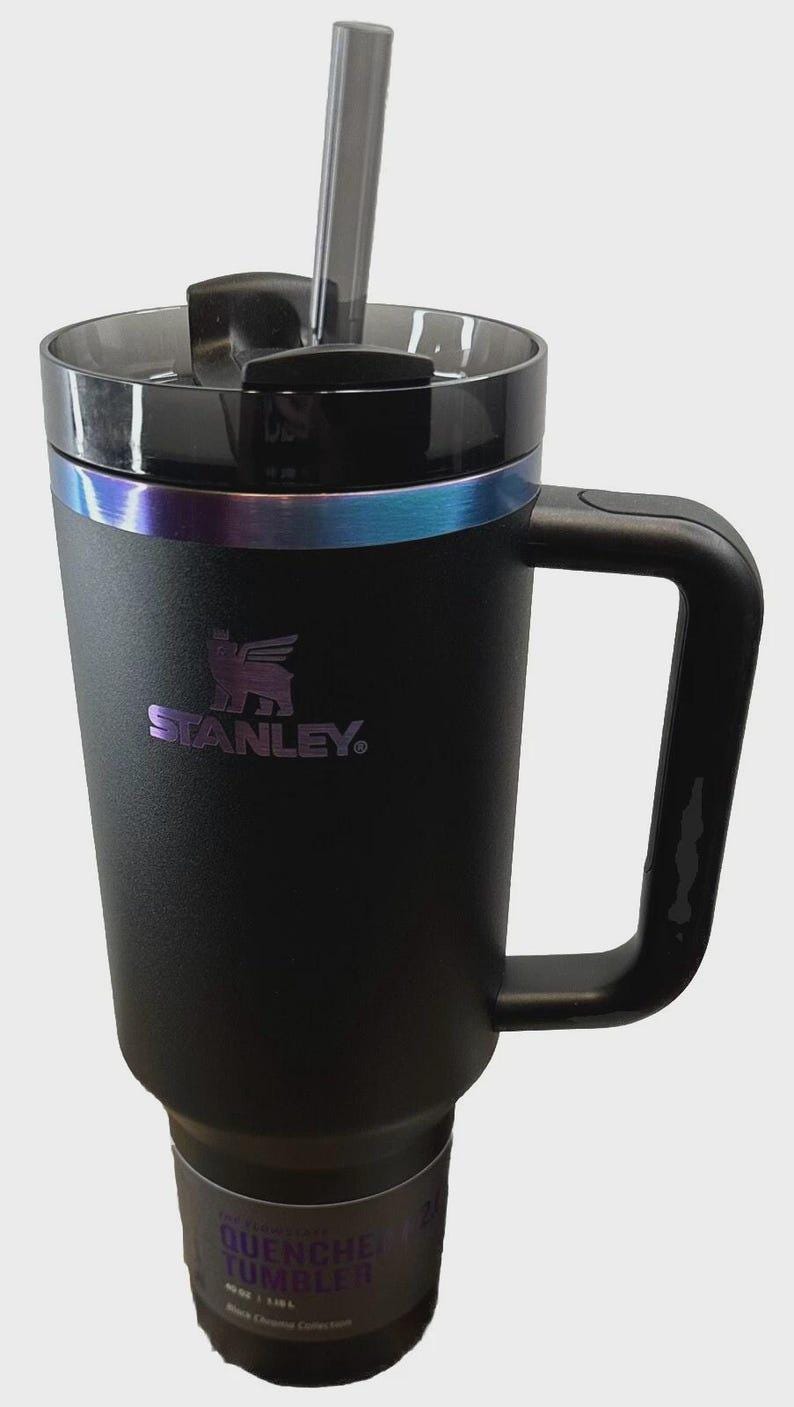 May include: Black Stanley Quencher tumbler with a handle and a clear straw. The tumbler has a black lid and a band of iridescent color around the middle. The Stanley logo is visible on the front.
