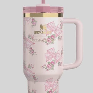 May include: A pink insulated travel mug with a handle, lid, and straw. The mug is patterned with pink bows and roses. The lid has a gold rim and a pink bow. The text "STANLEY LOVESHA" is visible on the mug.