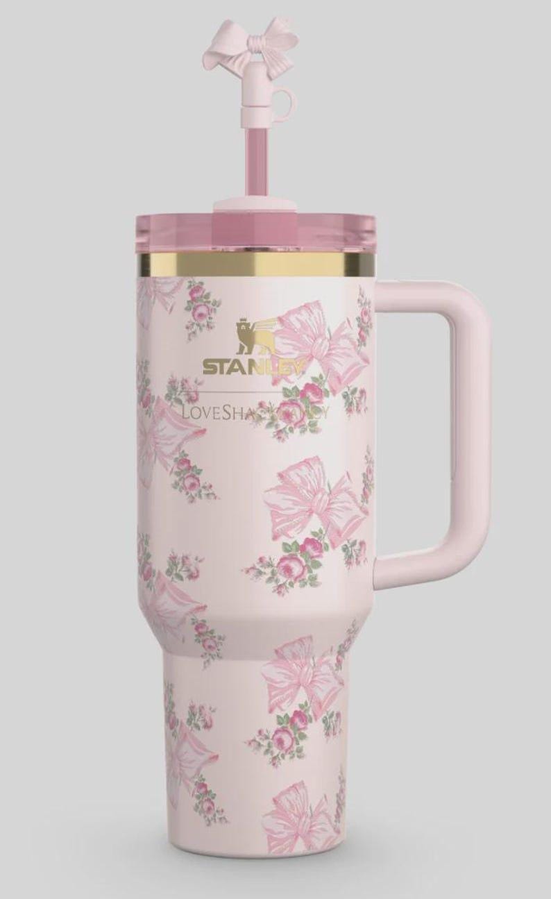 May include: A pink insulated travel mug with a handle, lid, and straw. The mug is patterned with pink bows and roses. The lid has a gold rim and a pink bow. The text "STANLEY LOVESHA" is visible on the mug.