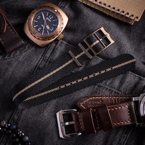 Pode incluir: Um relógio de pulso cor de bronze com mostrador preto exibindo o texto BOCTOK 1967, uma pulseira de nylon listrada em preto e bege com fivela de bronze e uma pulseira de couro castanho escuro separada com fivela de metal prateado.