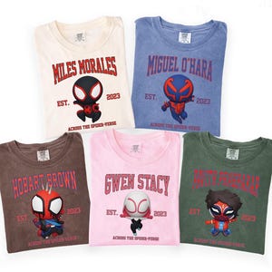 Puede incluir: Cinco camisetas en crema, azul, marr&oacute;n, rosa y verde, cada una con un personaje de Spider-Verse y su nombre. El texto incluye nombres de personajes, "EST. 2023" y "ACROSS THE SPIDER-VERSE".