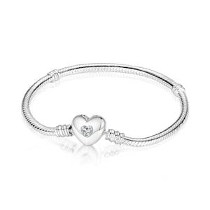 May include: A silver snake chain bracelet featuring a heart-shaped clasp. The clasp is polished silver and contains a small, clear, heart-shaped gemstone set in the center. The bracelet has two fixed stations along the chain for charm placement.