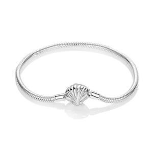 May include: A silver snake chain bracelet featuring a central clasp shaped like a seashell. The bracelet has a smooth, metallic finish and a circular design. The clasp is detailed with vertical ridges that mimic the appearance of a natural shell.