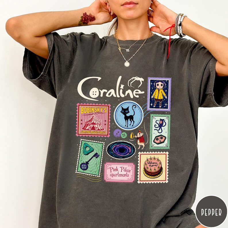 A person wearing a gray t-shirt with various colorful and whimsical images and text related to the movie "Coraline".