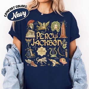 May include: Navy blue t-shirt with a graphic design featuring the text "Percy Jackson" and various illustrations, including a winged horse, a building, and a lyre. The shirt has a Comfort Colors label.