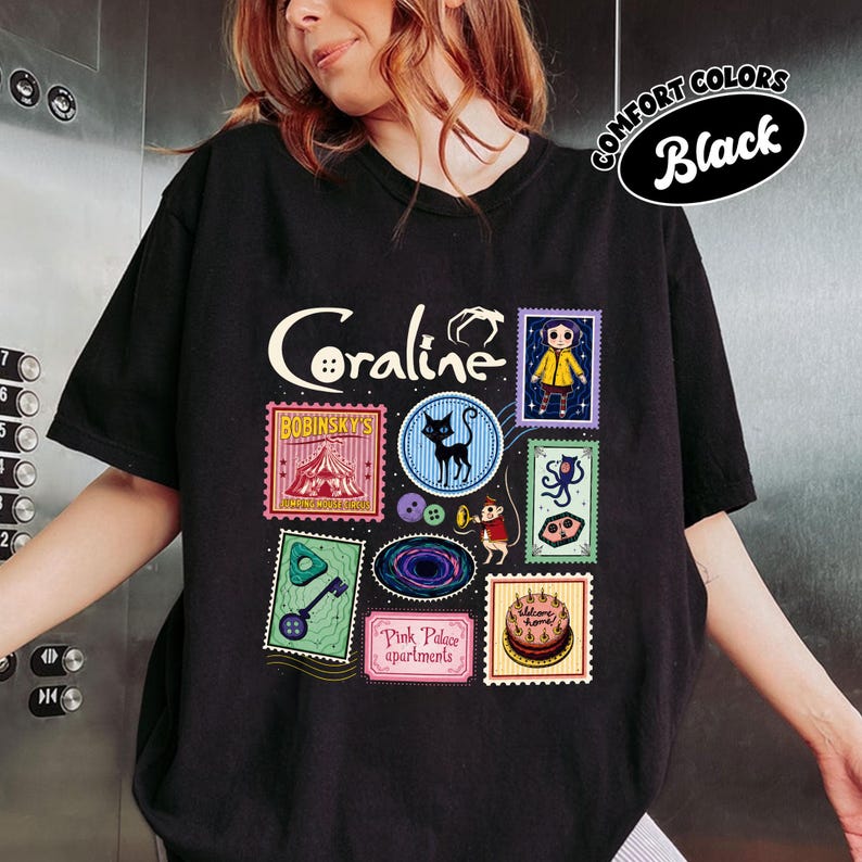 A person wearing a black t-shirt with various colorful and whimsical illustrations and text related to the movie "Coraline".