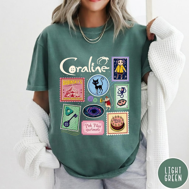 A woman wearing a green t-shirt with various colorful and whimsical illustrations, including a cat, a cake, and other decorative elements.