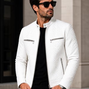 May include: A white, textured leather jacket with a stand-up collar and silver zippers. The jacket has a subtle pattern and is worn with a black shirt and black sunglasses. The jacket has two front pockets and a zipper closure.