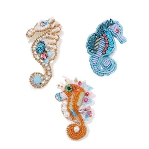 May include: Three beaded seahorse brooches in shades of blue, orange, and gold. Each brooch features intricate beadwork, sequins, and colorful gemstones. The seahorses are set against a white background.