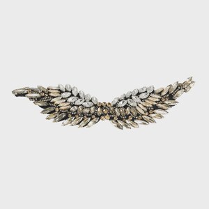 May include: A decorative wing-shaped accessory, adorned with clear and champagne-colored crystals. The crystals are arranged in a layered pattern, creating a sparkling effect. The base is a dark, possibly black, material.