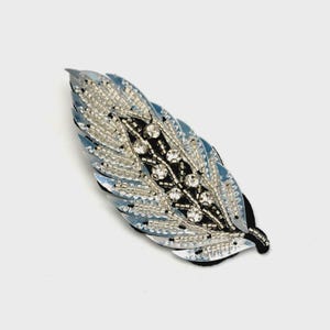 May include: A decorative feather-shaped embellishment. The feather features a light blue and silver sequined edge, with a black center adorned with clear rhinestones and silver beads. The item is designed for crafts or fashion.