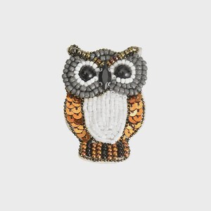 Puede incluir: Broche de búho con cuentas y lentejuelas. El búho tiene la cabeza gris, el pecho blanco y alas de lentejuelas doradas. Los ojos son negros y el pico es una pequeña cuenta negra. Accesorio decorativo.