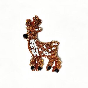 Könnte beinhalten: Ein dekorativer Hirsch-Anstecker mit braunen, goldenen, weißen und schwarzen Perlen. Der Hirsch hat einen braunen Körper, weiße Flecken und goldene Geweihe. Der Anstecker ist wahrscheinlich handgefertigt und für Kleidung oder Accessoires geeignet.