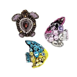 May include: Three beaded brooches: a turtle and two fish. The turtle brooch is dark purple with a red gem. One fish brooch is pink, black, and white with pearls. The other fish brooch is blue and yellow.