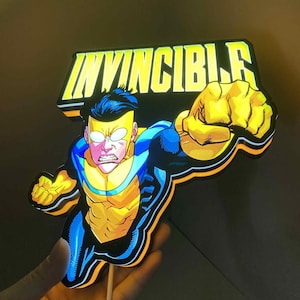 May include: A light-up sign displaying the word "INVINCIBLE" above a superhero character in a dynamic pose. The character is in a blue and yellow costume, with a clenched fist. The sign is held by a wooden stick.
