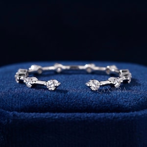 May include: A silver-toned open ring featuring a series of evenly spaced, round, clear faceted stones set along the band. The metal band has a polished finish, and the design includes a small gap at the front. The text LAXRA JEWELS is visible.