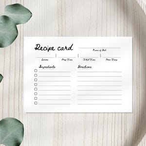 Può includere: Una scheda di ricetta bianca con le parole "Recipe card" in corsivo. La scheda ha sezioni per ingredienti e istruzioni, con caselle di controllo per ogni ingrediente. La scheda è su un vassoio di legno.