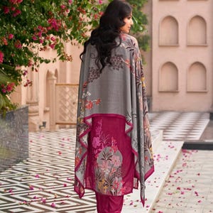 May include: A magenta tunic and matching trousers set featuring a floral print on the lower section, paired with a grey shawl that has a matching floral pattern along the edges. The ensemble is worn with light-colored heeled sandals.