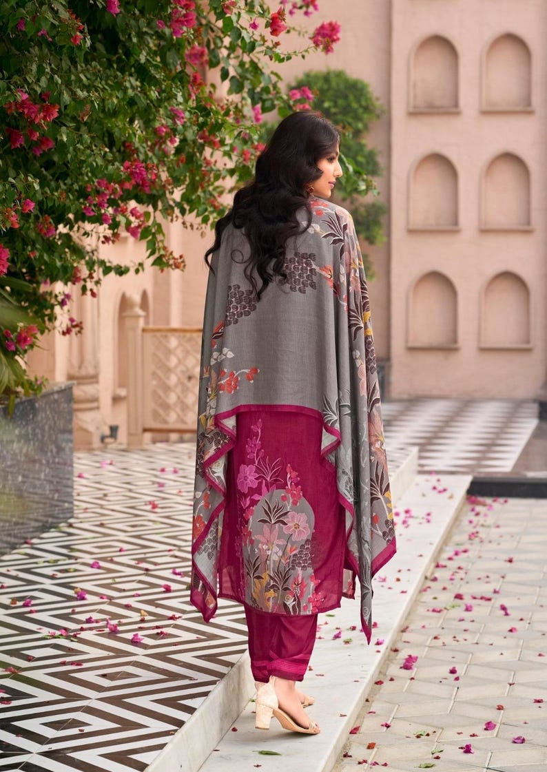 May include: A magenta tunic and matching trousers set featuring a floral print on the lower section, paired with a grey shawl that has a matching floral pattern along the edges. The ensemble is worn with light-colored heeled sandals.