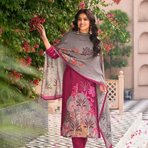 May include: A magenta tunic and matching trousers paired with a grey shawl. The tunic features a large, multi-colored floral print in shades of pink, orange, and white. The grey shawl has a matching floral pattern along the edges and hem.