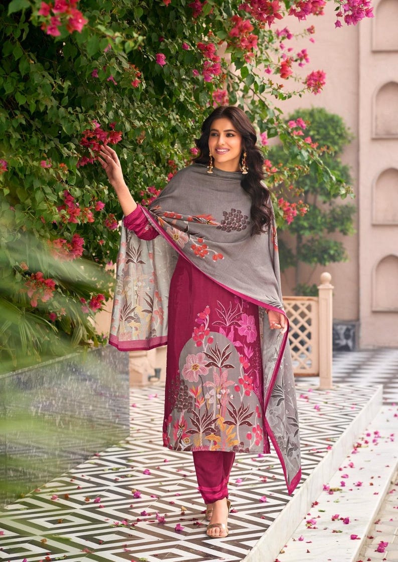 May include: A magenta tunic and matching trousers paired with a grey shawl. The tunic features a large, multi-colored floral print in shades of pink, orange, and white. The grey shawl has a matching floral pattern along the edges and hem.