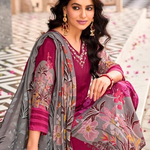 May include: A magenta long-sleeved tunic with a V-neckline featuring white embroidery, paired with a matching magenta pant and a grey shawl. The shawl is decorated with a large-scale floral print in shades of pink, orange, and dark green.