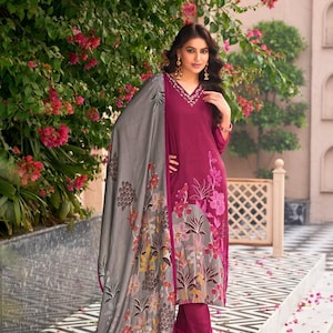 May include: A magenta long-sleeved tunic with a V-neckline featuring white embroidery, paired with matching magenta trousers and a large grey shawl. The shawl and the lower portion of the tunic are decorated with a multi-colored floral print pattern.