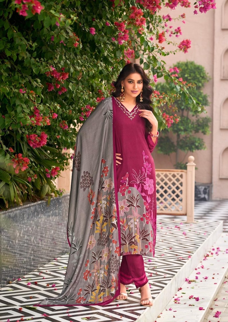 May include: A magenta long-sleeved tunic with a V-neckline featuring white embroidery, paired with matching magenta trousers and a large grey shawl. The shawl and the lower portion of the tunic are decorated with a multi-colored floral print pattern.