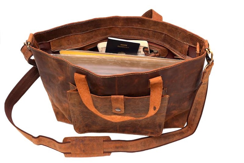 May include: Open brown leather tote bag with a front pocket and shoulder strap. The bag is filled with items, including a passport and files. The bag has a distressed look.