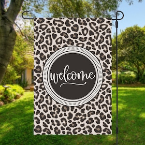 May include: A welcome garden flag with a leopard print background and a black circle with the word "welcome" in white script.