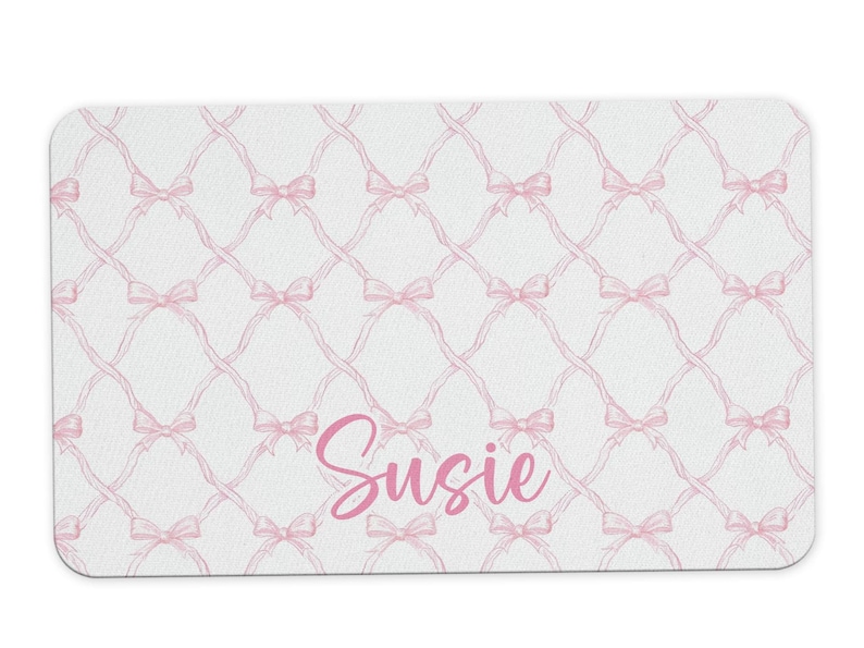 May include: A white doormat with a pink bow pattern and the name "Susie" written in pink.