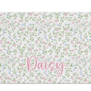 May include: A white bath mat with a floral pattern in pink and blue. The name "Daisy" is written in pink cursive lettering.