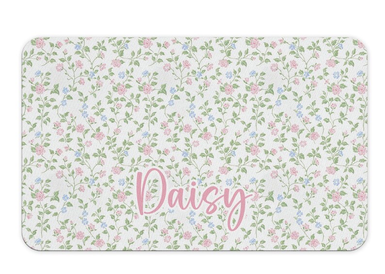 May include: A white bath mat with a floral pattern in pink and blue. The name "Daisy" is written in pink cursive lettering.