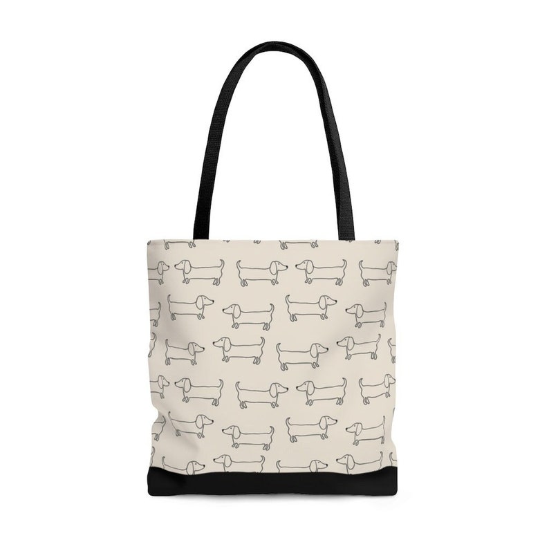 Op de afbeelding: Een beige tote bag met zwarte hengsels en een herhalend patroon van zwarte teckel silhouetten.