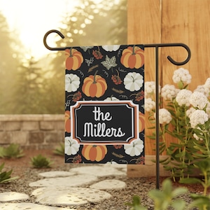 May include: A black garden flag with a fall theme featuring pumpkins and gourds. The flag has a white border and the text "the Millers" in a white font.