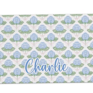 May include: A white rectangular doormat with a blue and green floral pattern and the name "Charlie" in blue script.