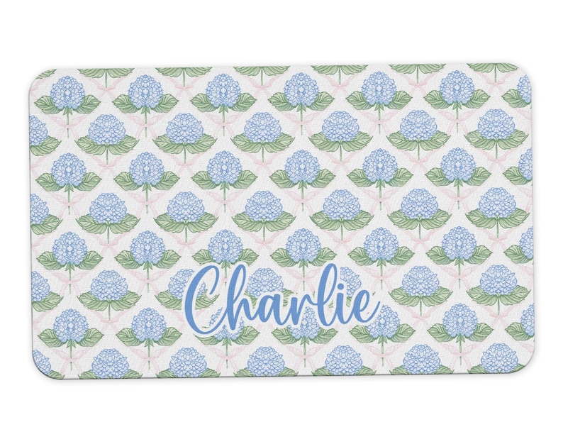 May include: A white rectangular doormat with a blue and green floral pattern and the name "Charlie" in blue script.