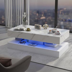 May include: A rectangular coffee table with a white faux marble top and a solid white base. The table features a central open storage compartment illuminated by blue LED lighting. The surface holds a book, a cup, a clock, and a small figurine.