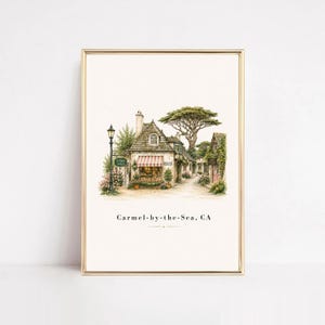 May include: A framed art print featuring a watercolor illustration of a quaint cottage with a red and white striped awning, a tall street lamp, and a large tree. The text "Carmel-by-the-Sea, CA" is printed in black at the bottom of the image.