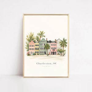 May include: A framed watercolor art print featuring a row of colorful historic houses in Charleston, South Carolina. The buildings are painted in shades of pink, yellow, and green with black shutters, surrounded by palm trees and greenery.