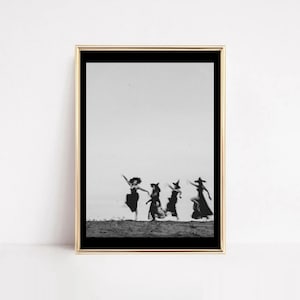 May include: Black and white framed print featuring a vintage photograph of four figures dancing. The figures are silhouetted against a bright background, with the print framed in a gold-colored frame. The figures are wearing long dresses and hats.