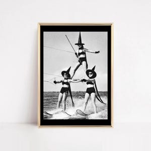 May include: Black and white framed print featuring three people water skiing in a pyramid formation. They are wearing witch hats and swimsuits. The image is a vintage photograph.