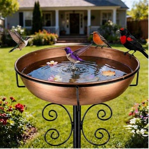 May include: A copper-colored bird bath with a decorative black metal stand. Several birds, including hummingbirds, are perched on the edge or flying near the water-filled basin. The bird bath is set in a garden with flowers and a house in the background.