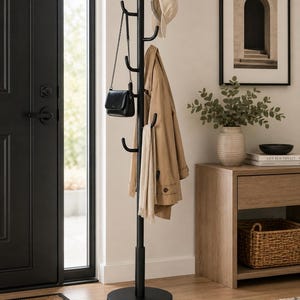 Puede incluir: Un perchero de metal negro mate con un poste vertical central y múltiples ganchos curvos. El soporte tiene una base circular y actualmente sostiene una gorra de béisbol beige, una gabardina color canela, una bufanda y un bolso de mano negro.