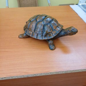 Op de afbeelding: Een bruin en zwart schildpadbeeldje met een getextureerd, gesegmenteerd schild en een gedetailleerde kop. Het beeldje heeft een realistische uitstraling met donkere schaduwen tussen de schildplaten en een gladde nek en poten.