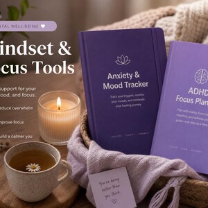 May include: Two hardcover journals in shades of purple, one labeled Anxiety & Mood Tracker and the other ADHD Focus Planner, featuring white text and line art icons. The journals are placed in a woven basket with a soft fabric.